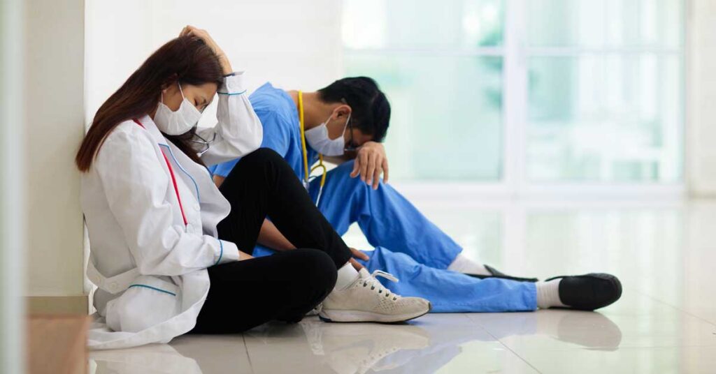 Two burnt out doctors sitting against a wall