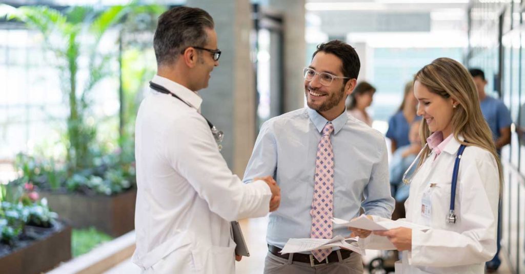 Two doctors and a businessman shaking hands in a hospital setting