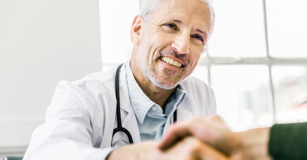 Smiling male doctor shaking hands with a patient