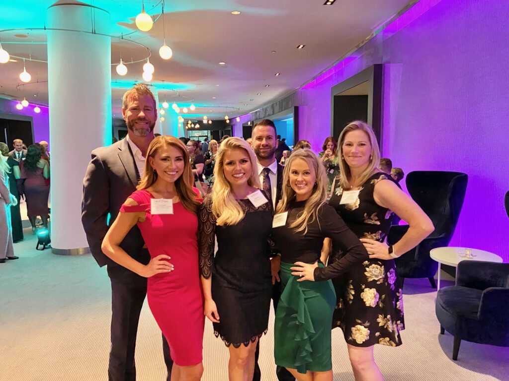 A group of six people dressed formally, smiling at the camera during a social event