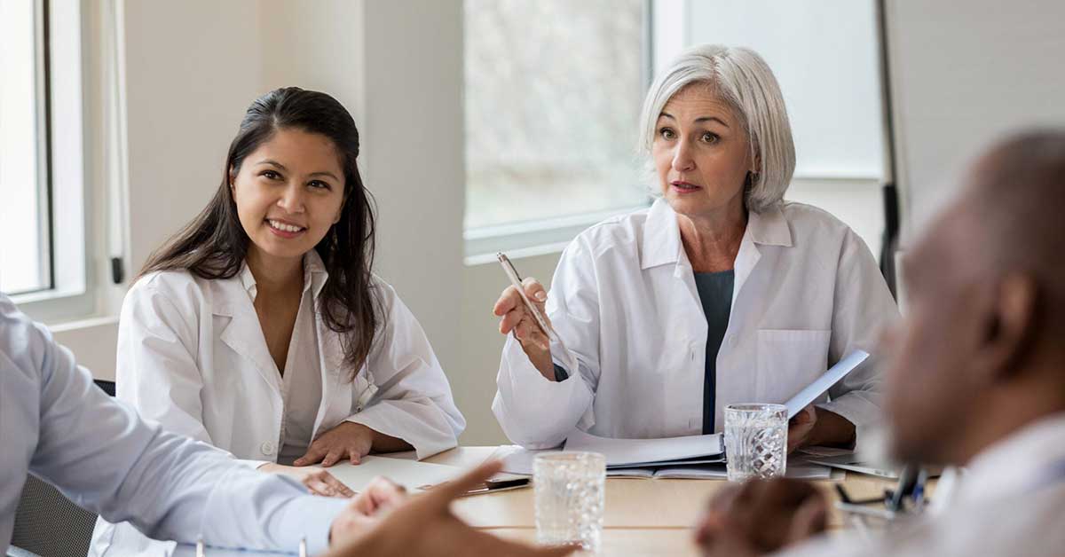 Team of healthcare workers in boardroom with female doctor presenting her plan