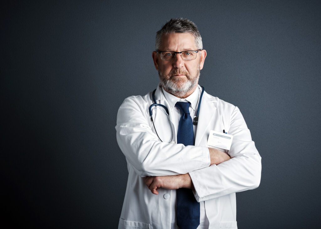 Confident doctor with glasses, arms crossed, standing against a dark background