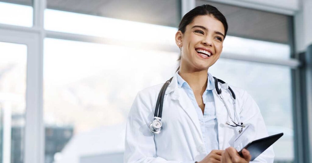Smiling female doctor holding a tablet, with a stethoscope around her neck