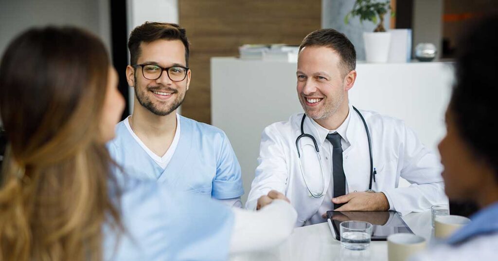 Smiling medical doctor shaking hands with another doctor during the meeting