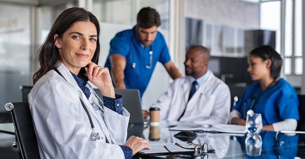 Doctor smiling at camera with colleagues discussing in background