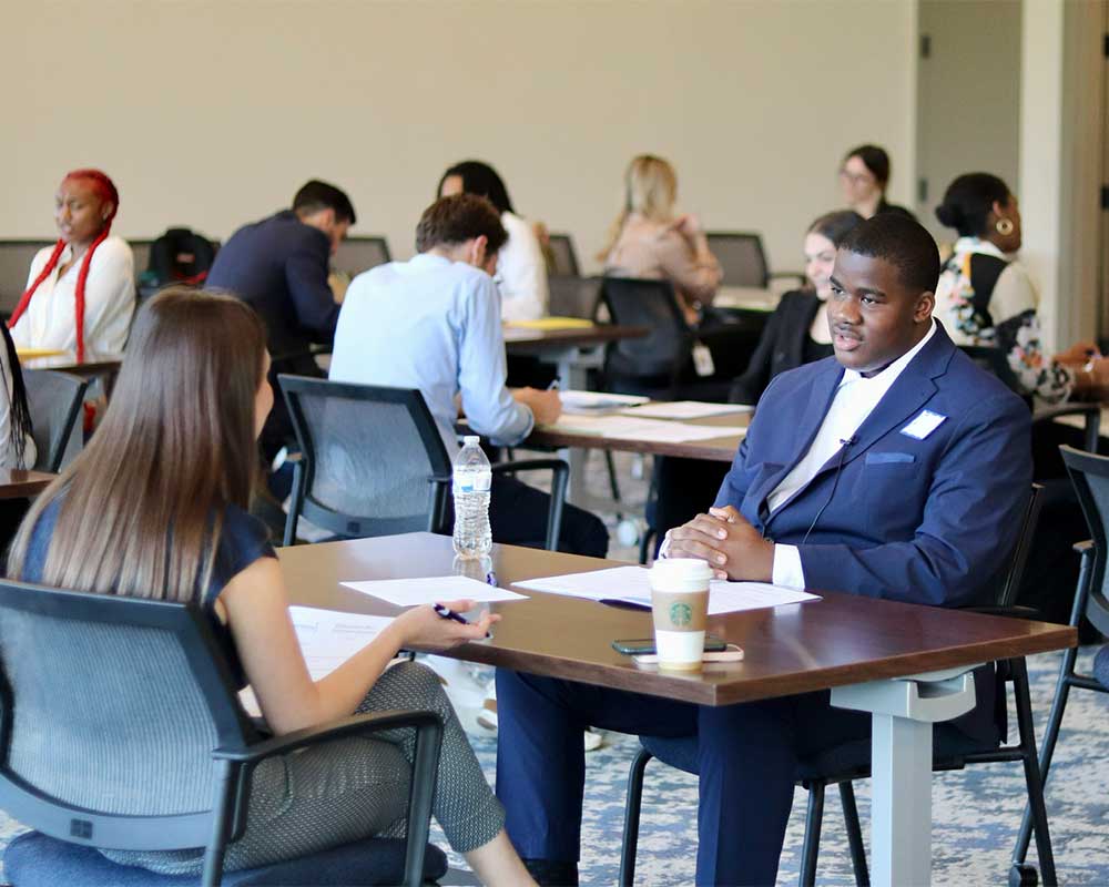 People participating in a professional interview with one person in a suit and others working in the background at different table