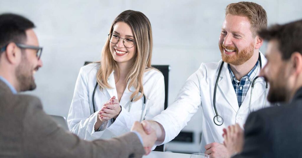 Doctors smiling and shaking hands with professionals in a meeting