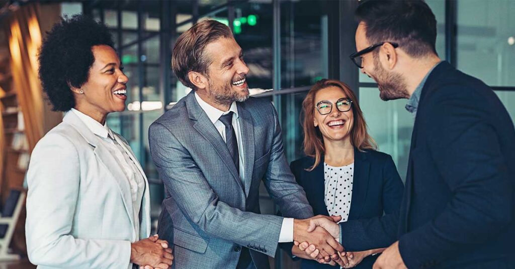 Business professionals smiling and shaking hands in a modern office setting