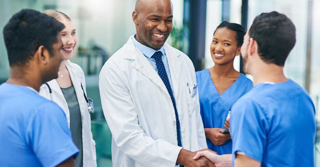 Smiling doctor shaking hands with a colleague surrounded by a diverse medical team