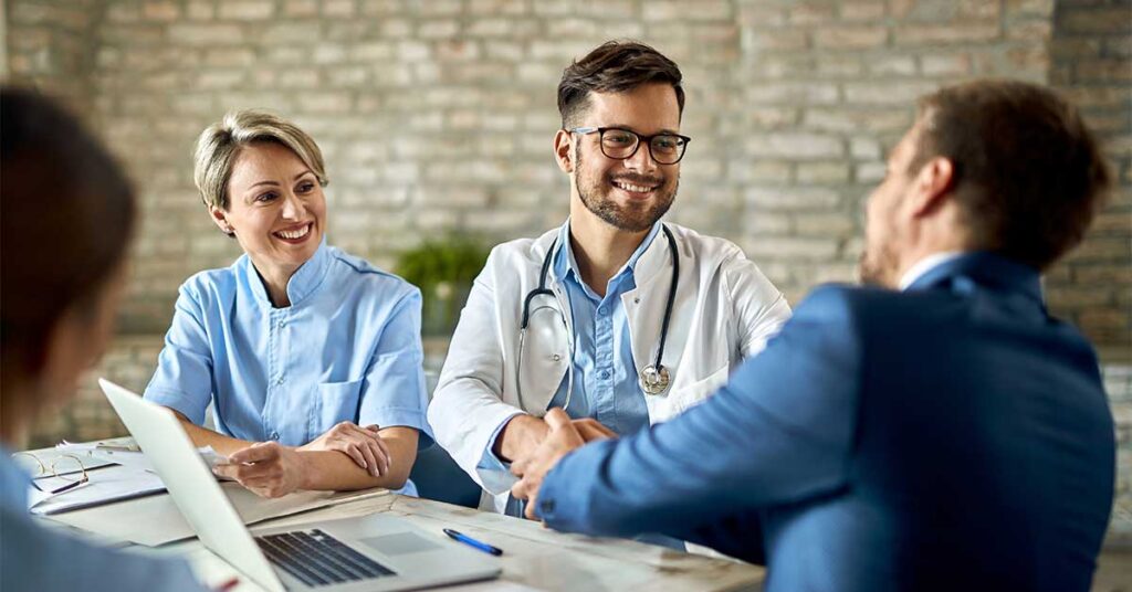 man shaking a doctor's hand in front of a laptop