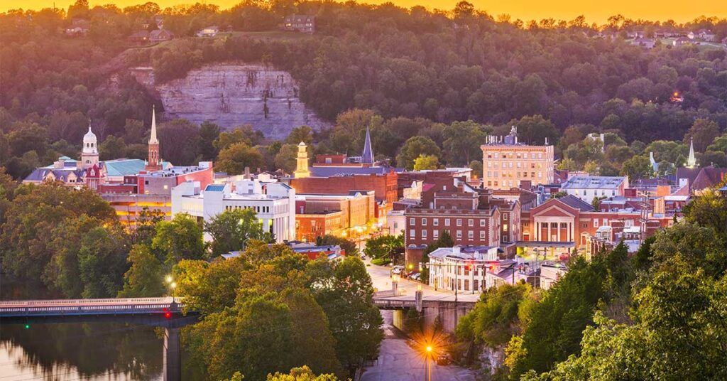 Aerial view of a small town in a valley at sunset, with buildings, church steeples, and surrounding green hills