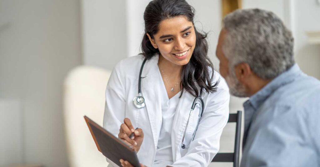 Female doctor smiling while showing a tablet to an elderly male patient