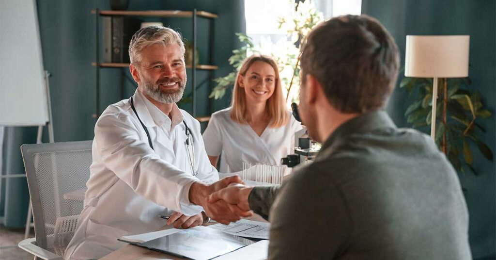 Doctor shaking hands with a patient during a consultation while a nurse smiles in the background