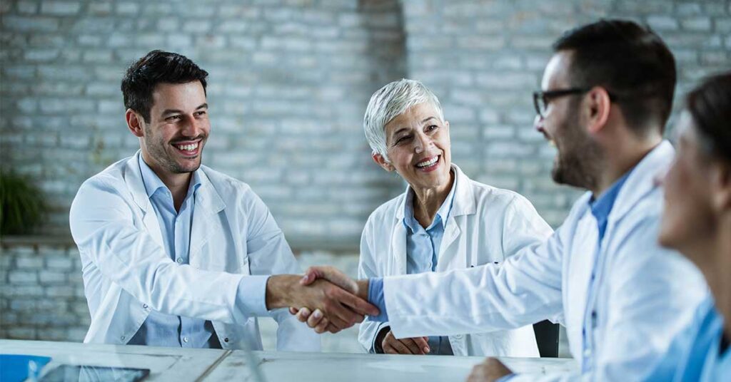 Doctors in white coats shaking hands and smiling during a collaborative meeting