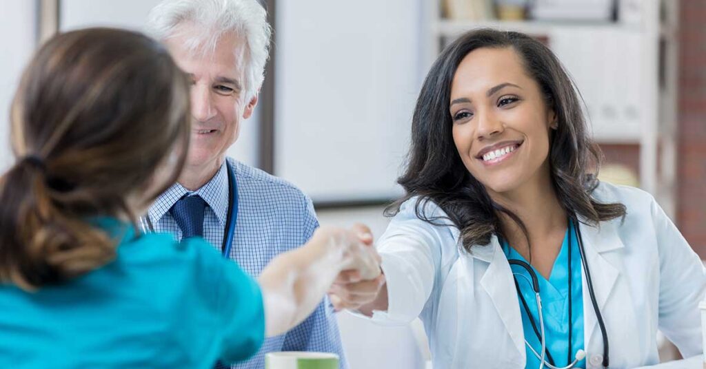 Smiling female doctor handing a document to a colleague while another doctor observes