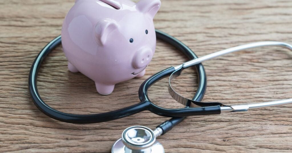 Pink piggy bank on a wooden surface with a stethoscope wrapped around it