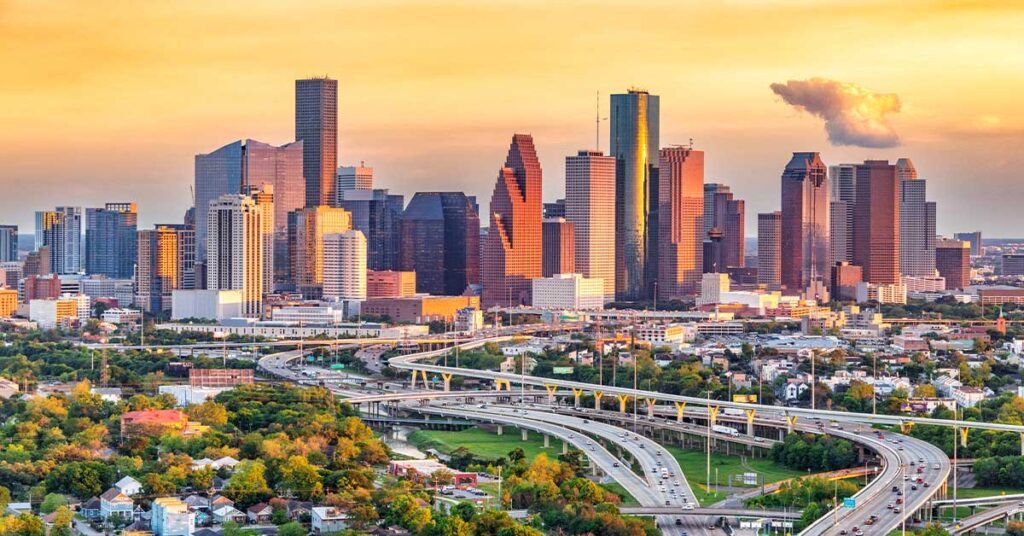 Cityscape with skyscrapers, highways, and a warm sunset sky
