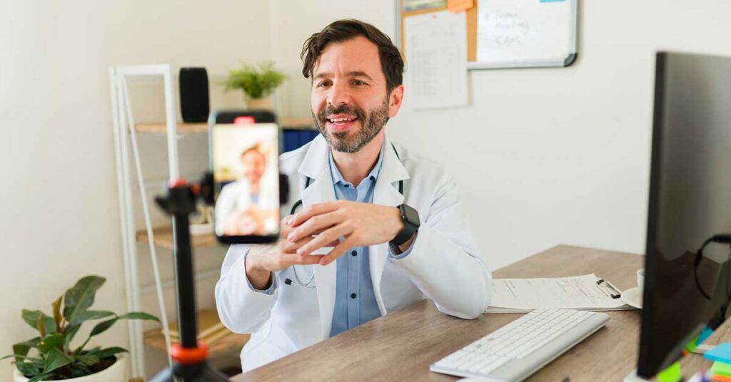Doctor with a lab coat at his office filming and streaming a medical video for social media with his smartphone