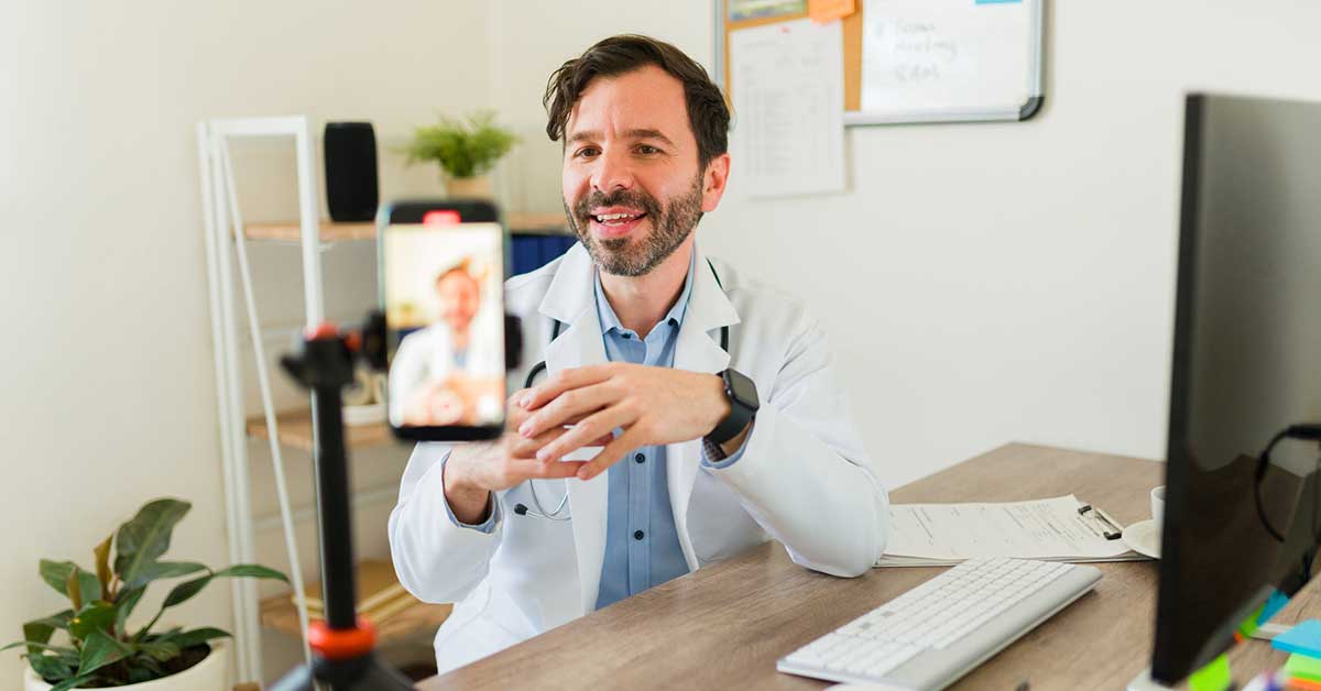 Doctor with a lab coat at his office filming and streaming a medical video for social media with his smartphone