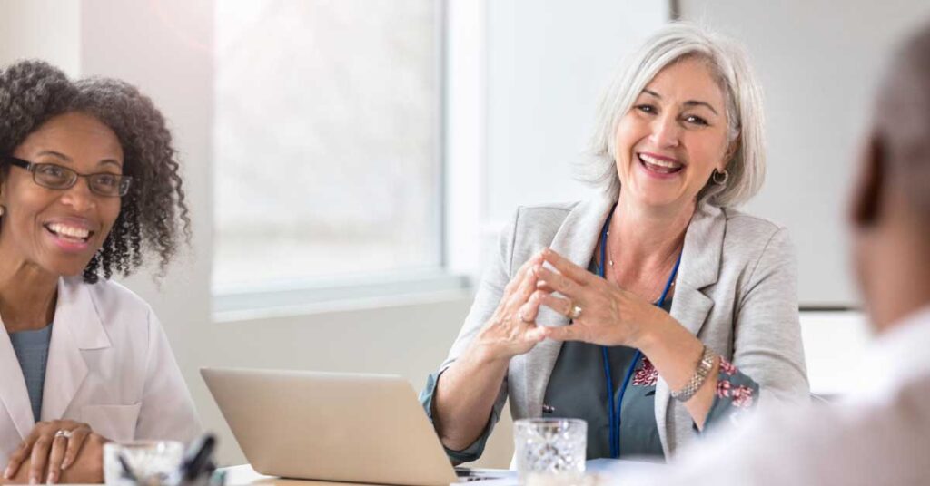 Mature Caucasian female hospital executive smiles and laughs as she talks with colleague
