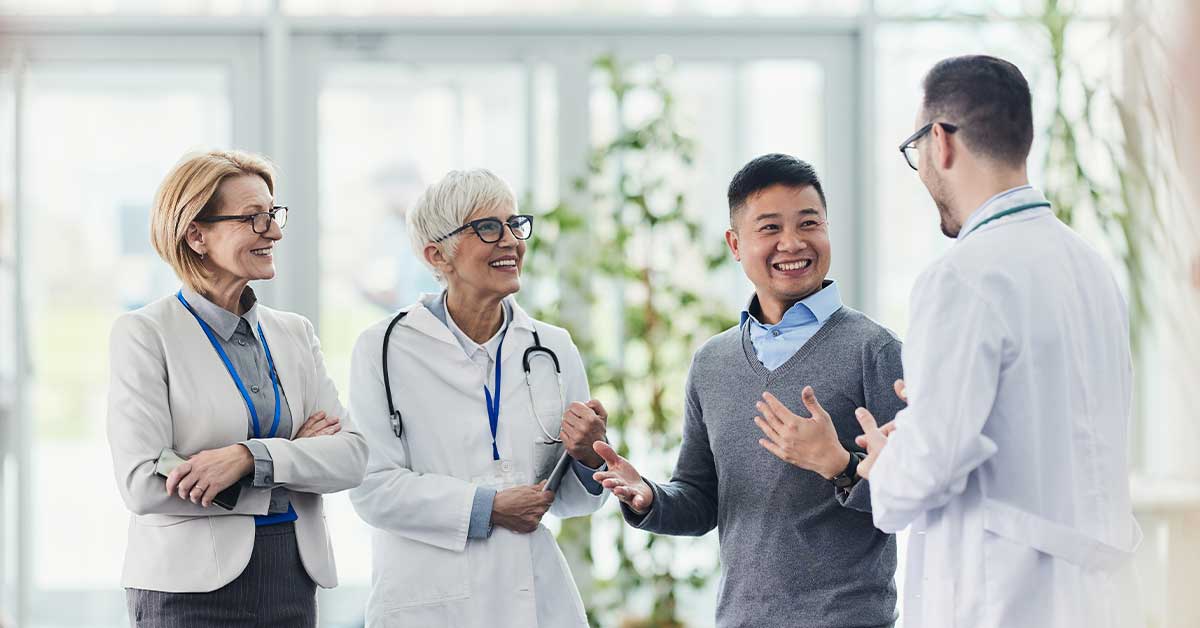 Happy medical experts communicating with two entrepreneurs in a hallway of a hospital.
