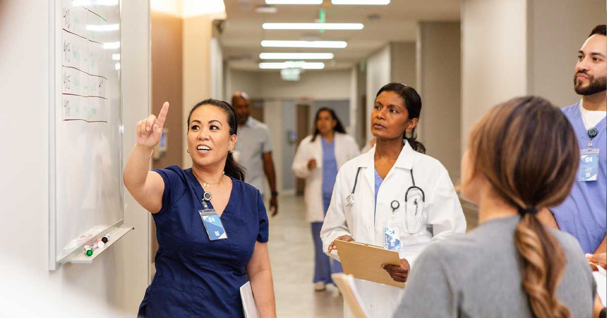 The young adult female nurse stands at the whiteboard to meet with her colleagues
