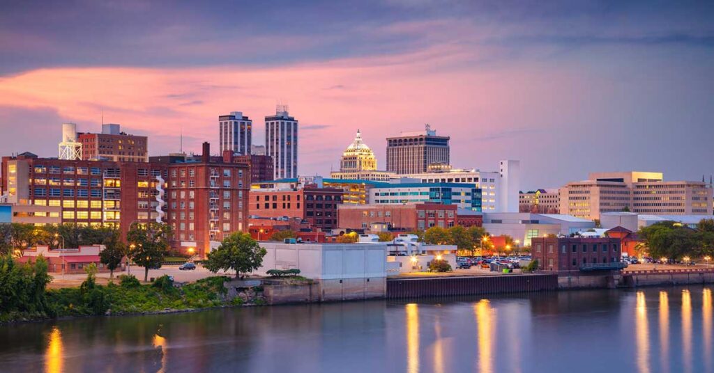eoria, Illinois during twilight blue hour features a skyline with illuminated buildings reflecting off a calm river.